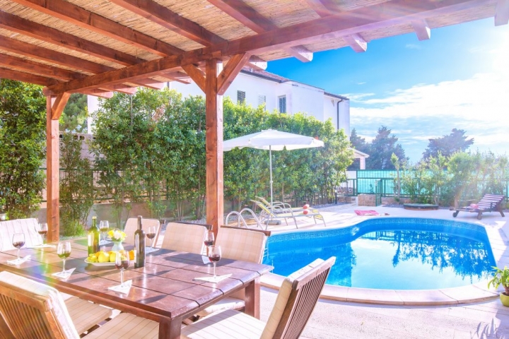 Covered outside dining table with the view on swimming pool and bed chairs with parasol